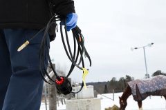Contractor holding Rizer-Line self-regulating heating cable outdoors at farm beside horse